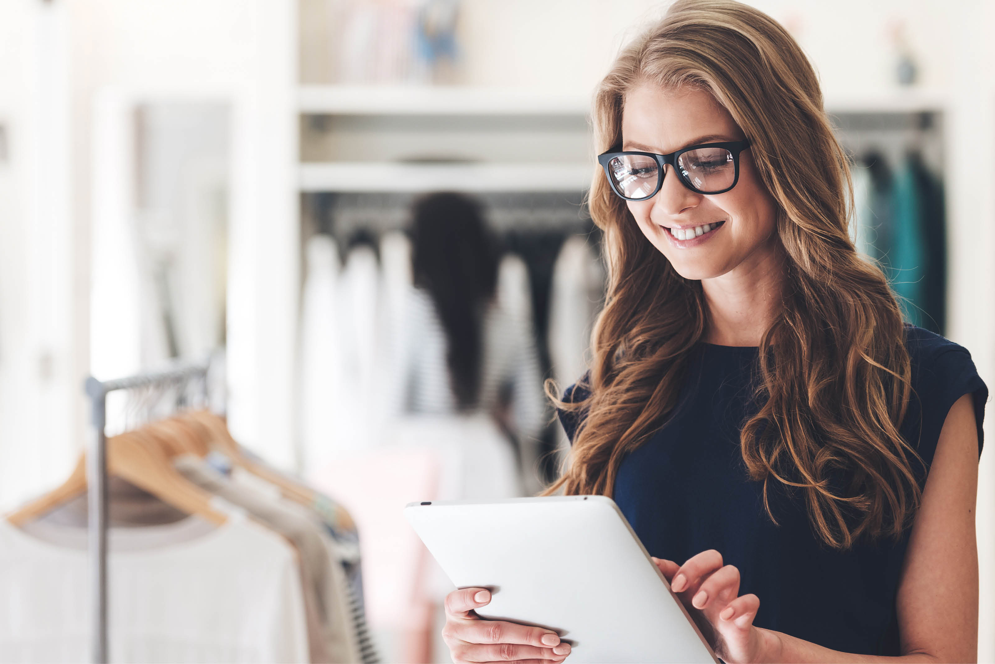 Starting new business. Beautiful young woman using digital tablet with smile while standing at the clothing store 