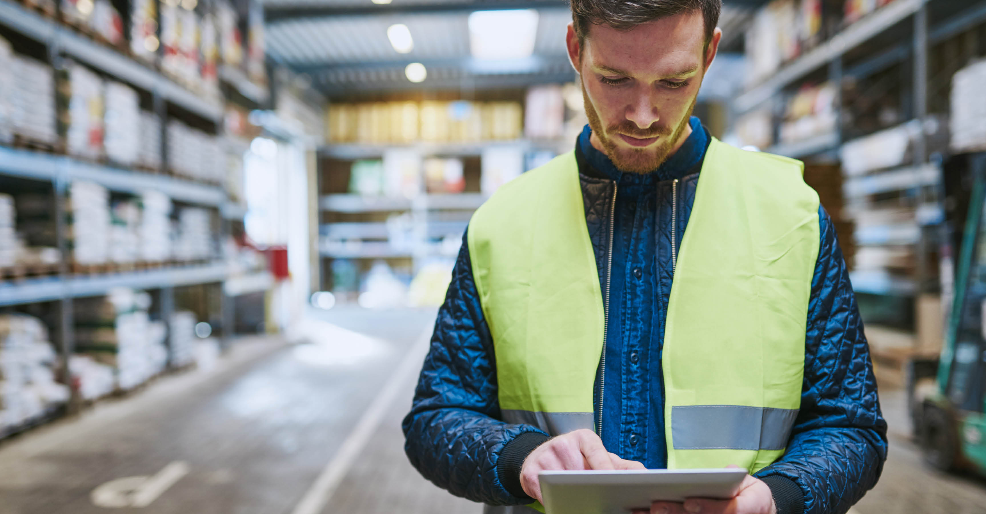 Young man looking up order details on a tablet as he shops in a hardware warehouse for supplies , close up upper body
