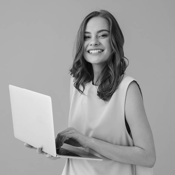 Image of cheerful young woman standing isolated over pink background using laptop computer. Looking camera.