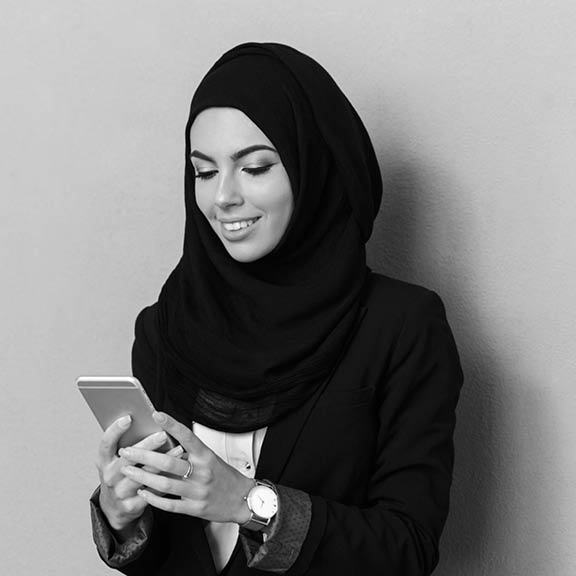 Portrait of a smiling young arabian woman using mobile phone isolated over gray background