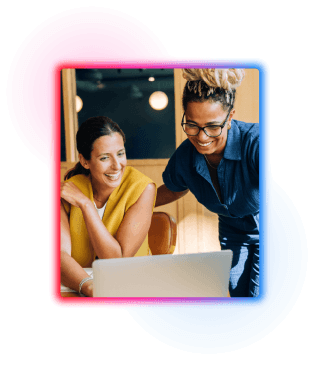 Two women, one sat down, the other standing looking at a laptop screen