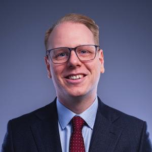 David Taylor, a smiling man wearing square glasses and a navy blue suit.