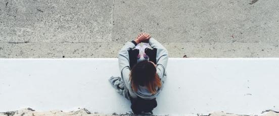 Aerial view of girl sat outside alone, on concrete