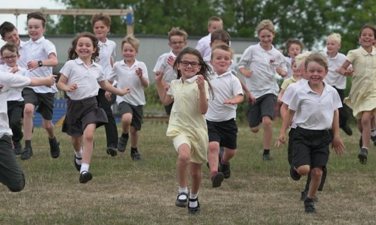 School kids running across a field looking happy