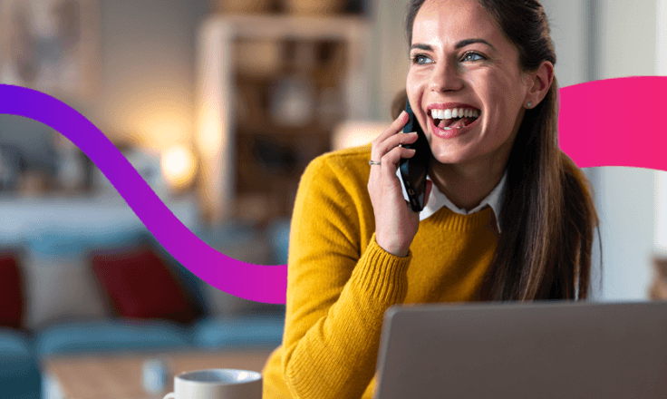 Women talking on the phone smiling, sat in front of a laptop