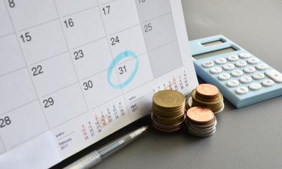 Calculator with coins and a calendar, signifying Tax Year End is imminent