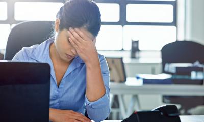 Woman sat at her desk, with her head in her hands, representing stress and pressure