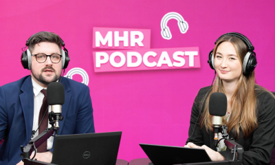 Alice and Andy sat with headphones on infront of a mic and laptop, with MHR podcast written behind them.