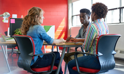 Three people sat on a table, taking notes, working in HR at MHR.