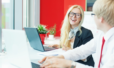 lady with glasses, laughing with a man who has a red tie on working on laptops helping people in managed services