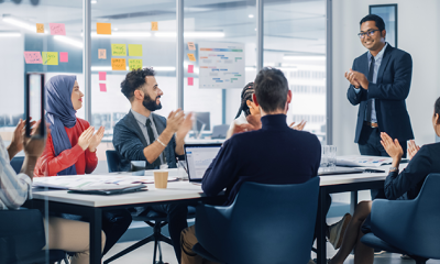 5 people sat at a table clapping to a person presenting at the front working in product design at MHR., 