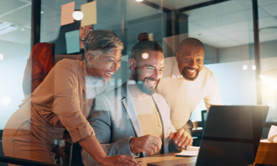 Three people sat around a laptop in an office, smiling.