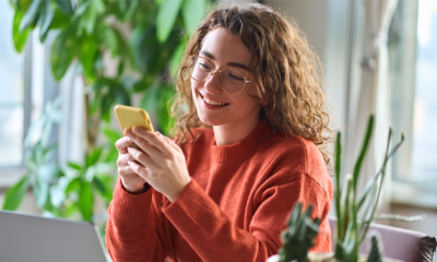 A remote worker, working from a coffee shop accessing People First from MHR on her mobile phone