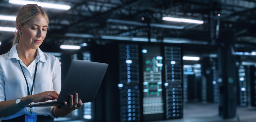 A lady in a warehouse, wearing office attire on her laptop.