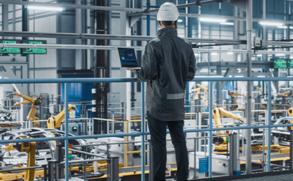 A worker in a manufacturing facility, overseeing the automated building of products