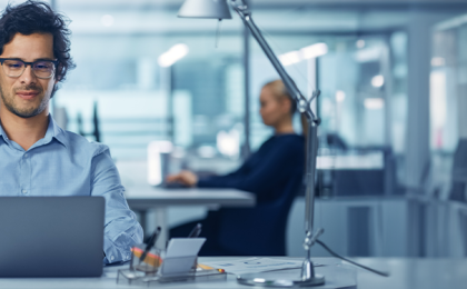a man sat at a desk working in a laptop managing his hr and payroll through MHR's software solutions.