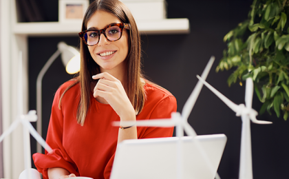 A lady sat at a desk, working on a laptop with windmills behind her.