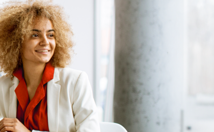 a lady sat at a table smiling, with two people behind her. Happy about People First's real-time payroll feature.