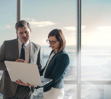 Two employees in suits looking at a laptop