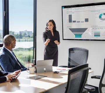 Image of two men and a woman in a meeting room with Microsoft Dynamics showing on a large screen