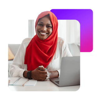 a lady sat down wearing a headscarf, working on a laptop smiling.