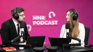 Alice and Andy sat with headphones on infront of a mic and laptop, with MHR podcast written behind them.