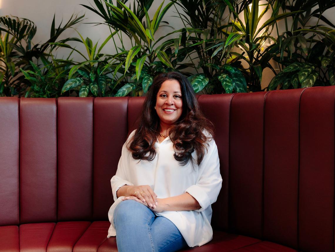 Nisha Marwaha sits on a red sofa.