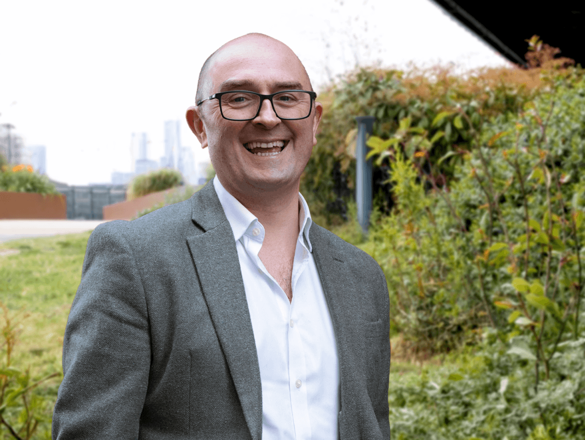 Tom Cheesewright smiles at the camera in front of a green field.