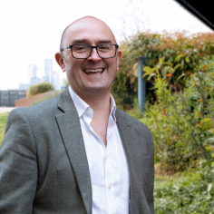 Tom Cheesewright smiles at the camera in front of a green field.