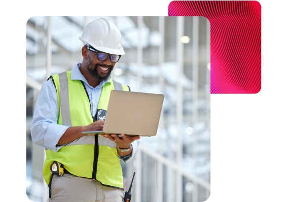 a man wearing a construction hard hat, holding a laptop. Checking into People First cloud-based platform, remotely.