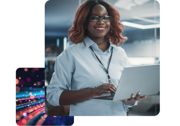 A lady stood in an office, holding a laptop smiling. 