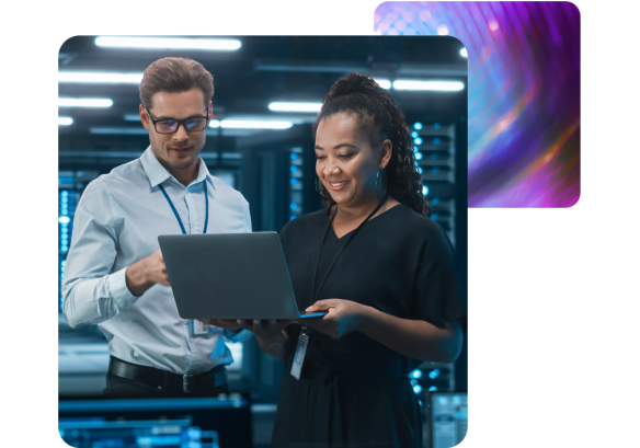 A man and a lady stood in server room looking at a laptop, doing some training.