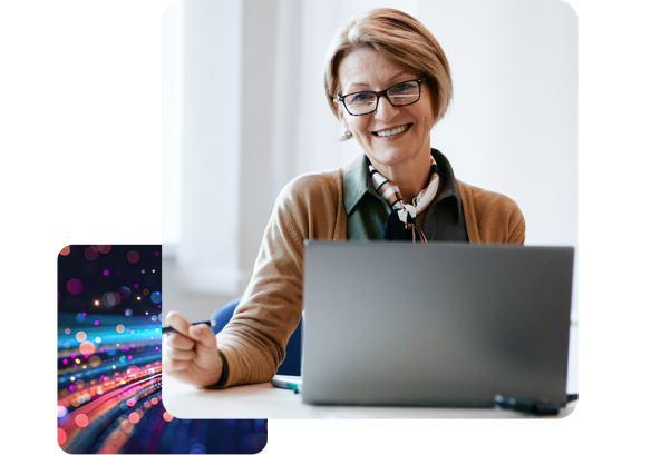 a lady sat at a desk, working on a laptop smiling.