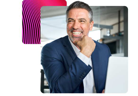 a man sat at a desk, smiling. working on a laptop.