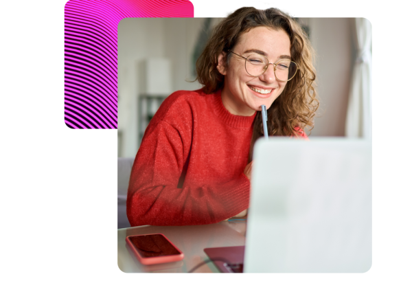 a lady smiling holding a pen, looking at a laptop. 