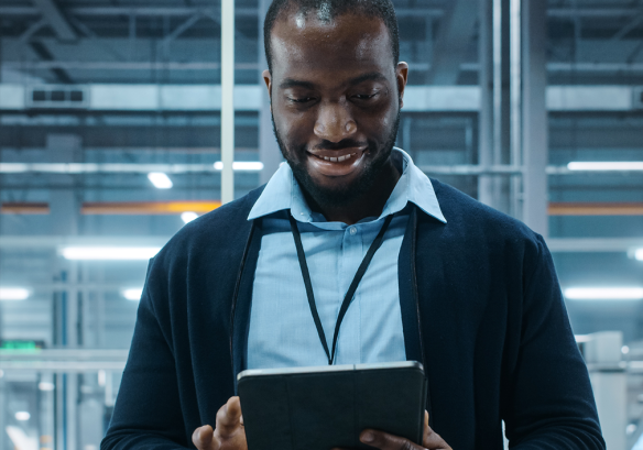 Man with lanyard in working environment looking at iPad and smiling