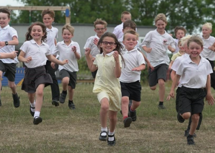 School kids running across a field looking happy
