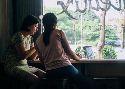 Two women sitting by a shop window with writing on it