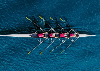 Aerial shot of 4 women, wearing pink t-shirts, rowing a scull boat.