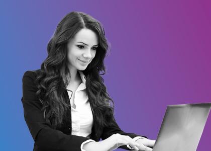 a lady in a suit, smiling, working on a laptop.