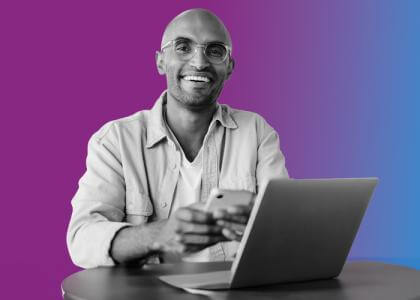 a man with glasses on his phone with a laptop in front of him. 