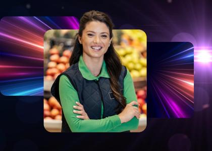 A retail worker in a green uniform, smiling with folded arms.