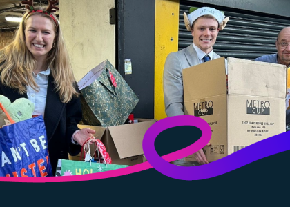 Three people holding gifts outside a donation drop off point at Christmas