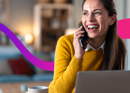 Women talking on the phone smiling, sat in front of a laptop