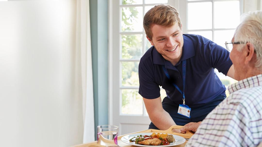 Healthcare worker serving elderly gentleman dinner