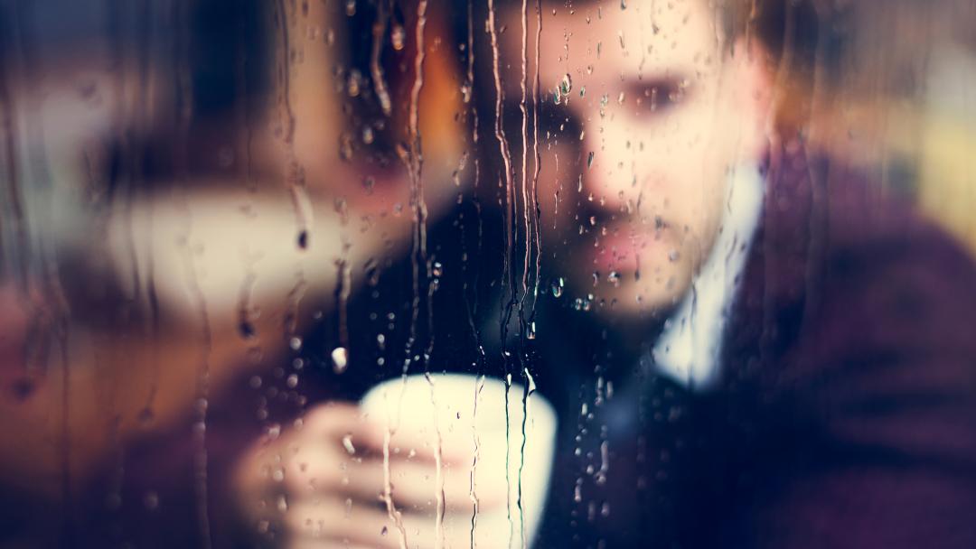 Sombre office worker looking out of the window and seeing rain outside