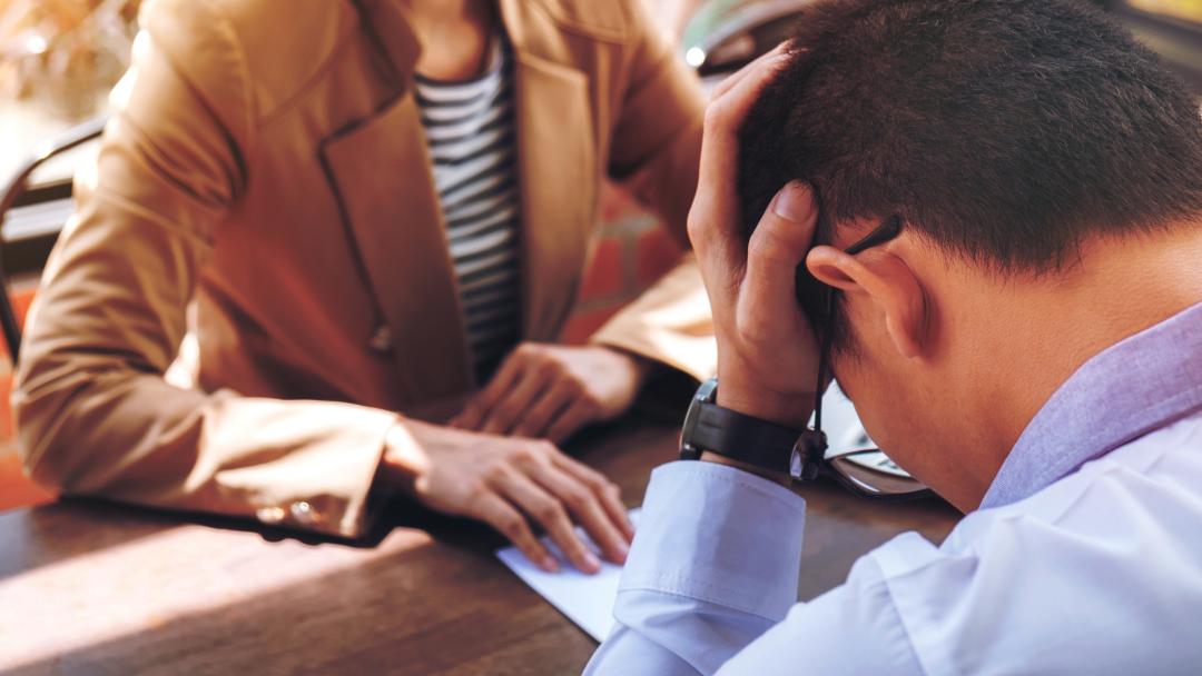 Employee with his head in his hands during a meeting with his manager