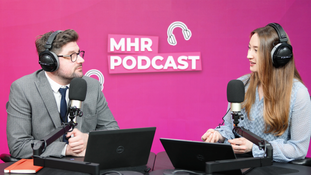 Alice and Andy sat with headphones on infront of a mic and laptop, with MHR podcast written behind them.