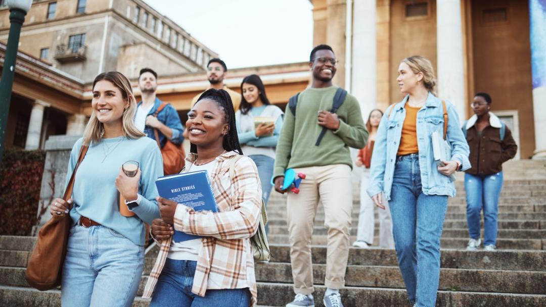 nine university students holding books, walking down steps.