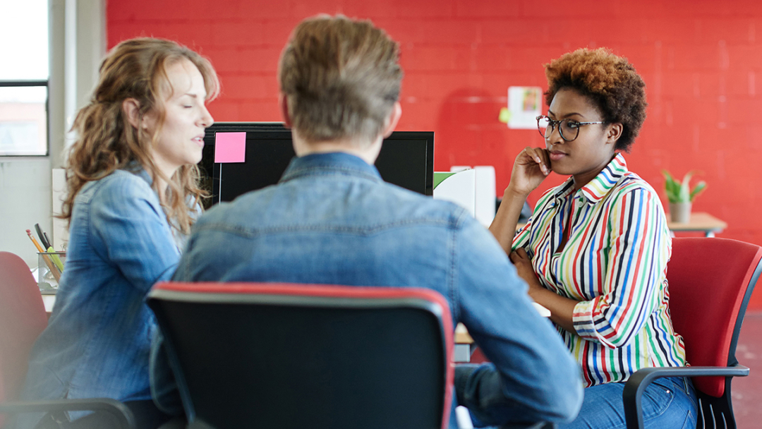A group of two women and a man sat at a table in an office environment